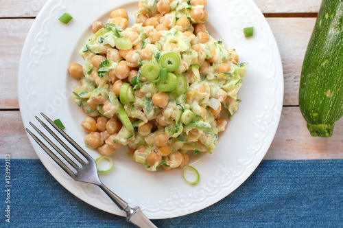 Healthy meal from chickpeas, zucchini, spring onion and cream on white plate with fork on wooden background