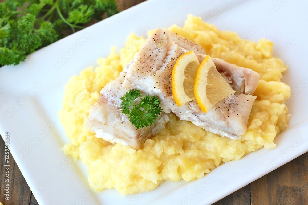 Healthy meal from fish and mashed potatoes with lemon and parsley on white plate on dark brown wooden background