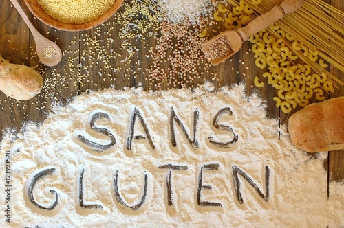 Gluten free cereals corn, rice, buckwheat, quinoa, millet, pasta and flour with text gluten free in French language on brown wooden background