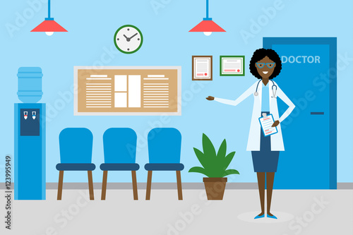 Doctor in waiting room. Beautiful smiling african american woman in white standing in waiting room. Hospital interior with chairs and health care information.