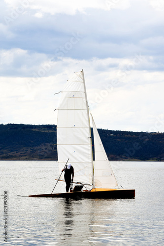 Man standing on a sail boat on a calm lake