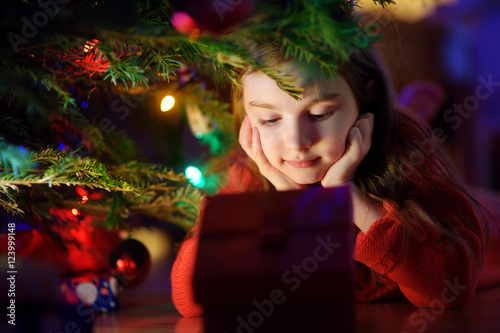 Adorable little girl looking for gifts under a Christmas tree