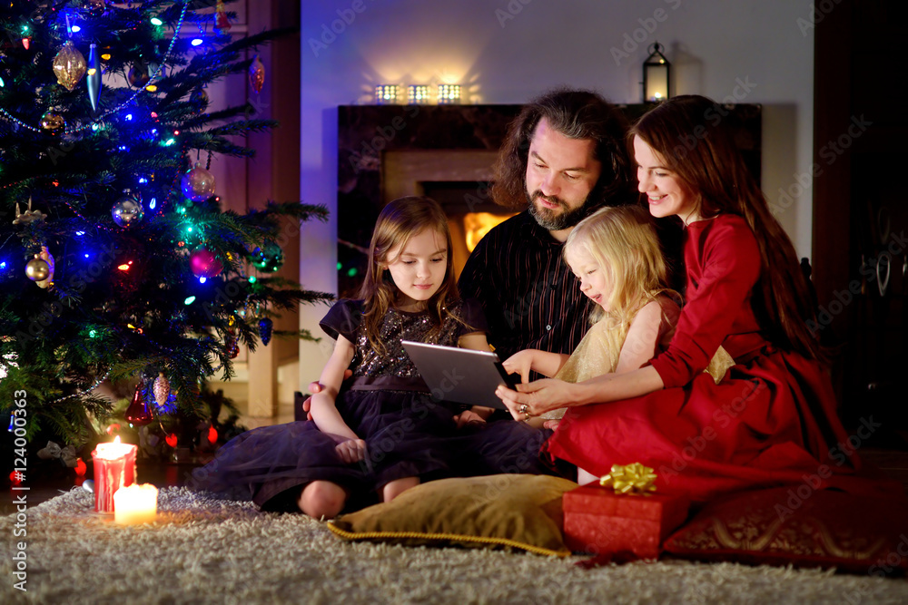 Happy young family using a tablet pc at home by a fireplace in warm and cozy living room