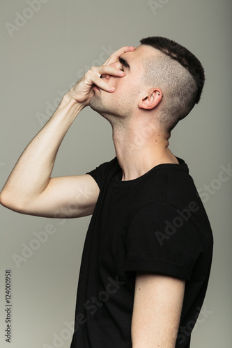 Side-view of man with shaven temples in black t-shirt, who feeling shame and holding his right hand on face. Isolated © kkolosov