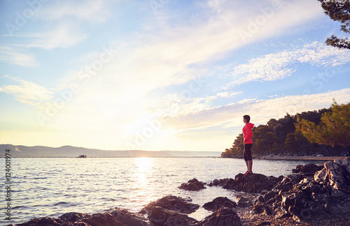 Runner resting from routine exercise. Happy jogger relaxing at the beach after run  standing on the stones and looking at the sea. Active young woman enjoying sunrise.