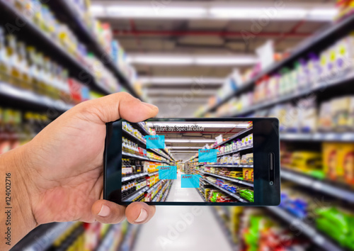 Augmented reality application for retail business concept. Hand holding smart phone with A/R application on screen to scanning sale alert in supermarket. 