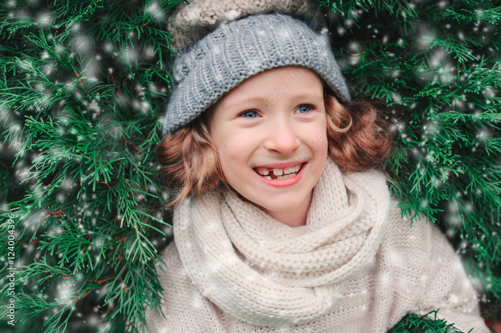 close up winter portrait of happy child girl wearing warm knitted hat and scarf with Christmas tree on background close up winter portrait of happy child girl wearing warm knitted hat and scarf with Christmas tree on background