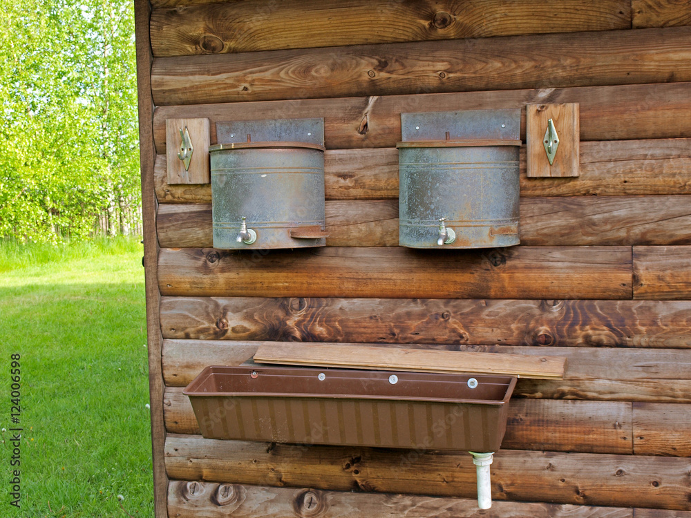 Sink and water tanks with taps on log house wall for washing outdoor Sink and water tanks with taps on log house wall for washing outdoor