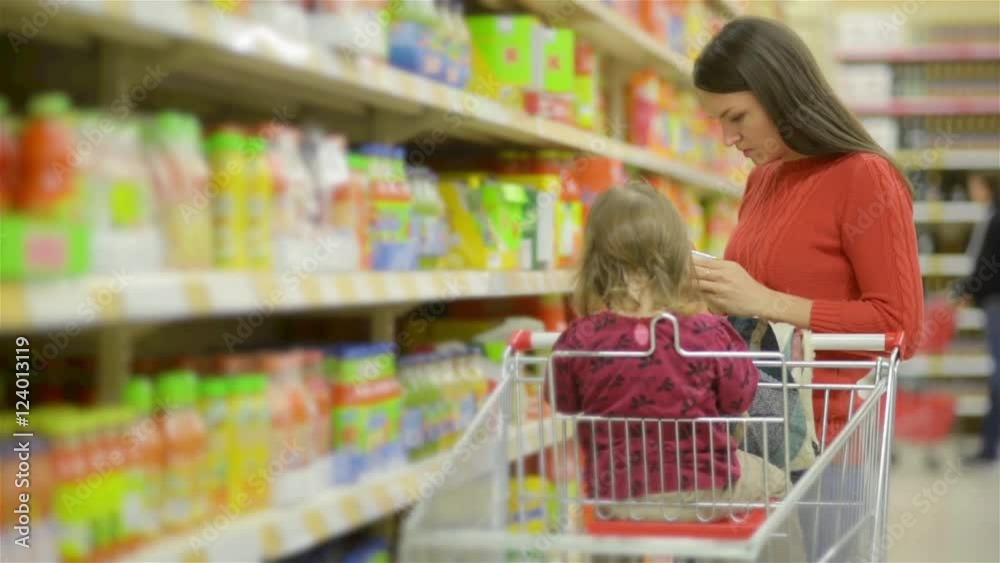 Mother and child walks along wholesale shelves and taking goods in shop trolley, beautiful young wife shopping in a supermarket Mother and child walks along wholesale shelves and taking goods in shop trolley, beautiful young wife shopping in a supermarket