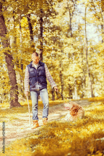 Young man walking a dog at the park in good weather. Boy and golden retriever.  Autumn environment © nikodash