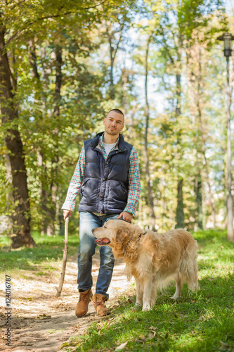 Young man walking a dog at the park in good weather. Boy and golden retriever. Autumn environment