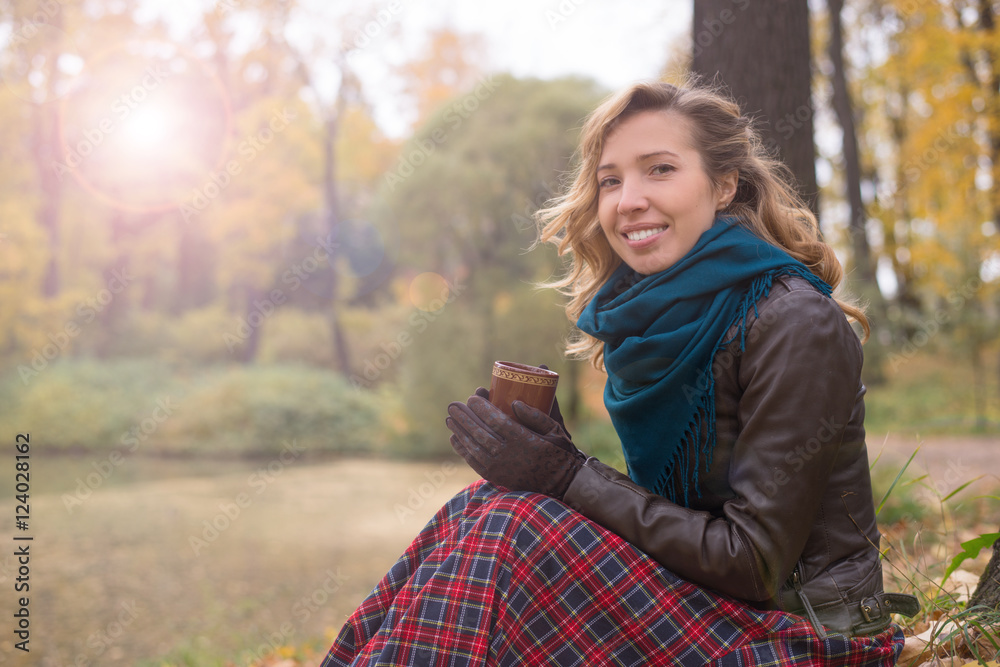 Beautiful girl blonde with wavy hair sitting in an autumn tree with yellow leaves with a cup of hot drink Beautiful girl blonde with wavy hair sitting in an autumn tree with yellow leaves with a cup of hot drink