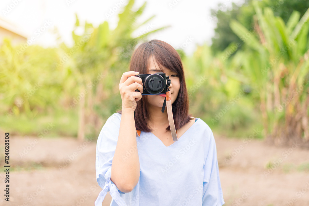Smiling young woman using a camera to take photo outdoors at the park