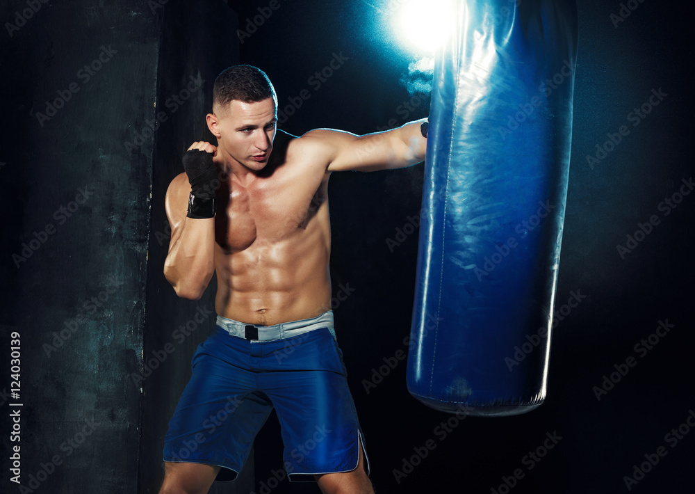 Male boxer boxing in punching bag with dramatic edgy lighting in a dark studio Male boxer boxing in punching bag with dramatic edgy lighting in a dark studio
