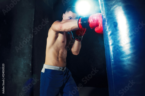 Male boxer boxing in punching bag with dramatic edgy lighting in a dark studio