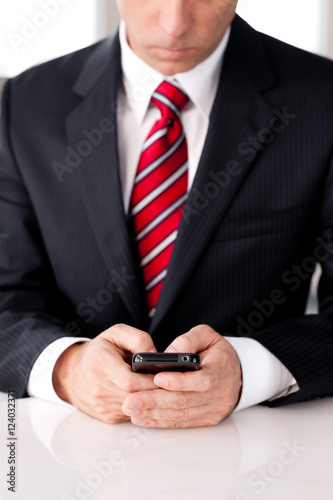 Businessman texting with mobile phone in bright office
