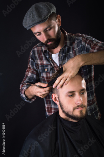 Barber cuts client with scissors hair. On a black background.