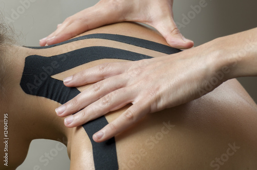 Physiotherapist putting on black kinesio tape on woman patients
