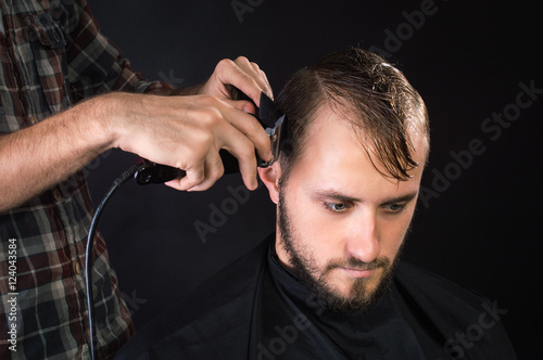 Barber shaves the hair to the client. On a black background.