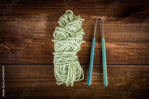 Green skein of knitting yarn. Green crochet hooks. On a wooden background. Top view. Flat lay.
