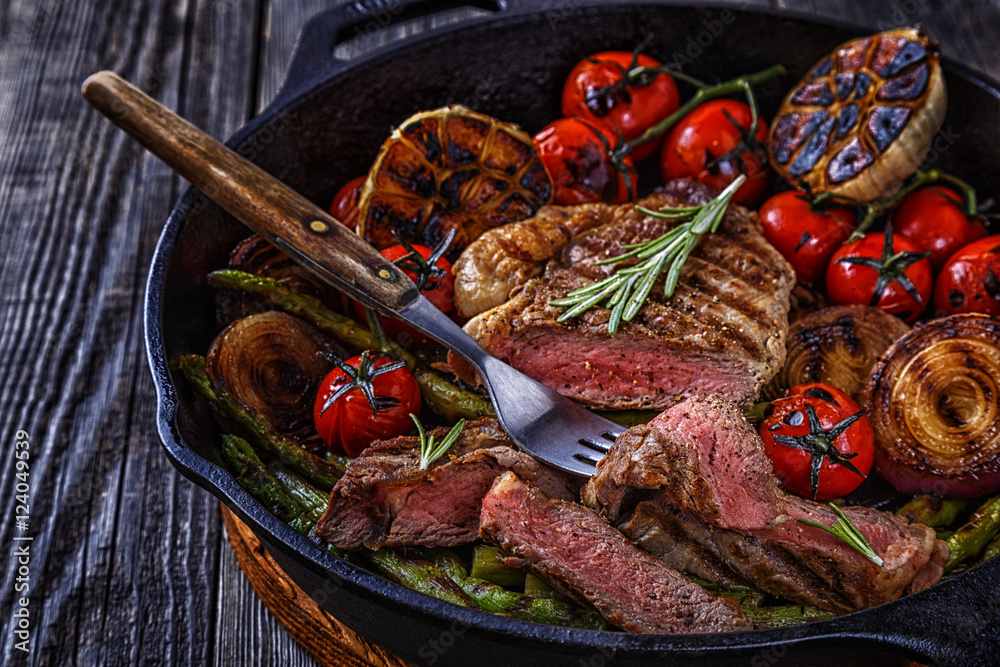 Steak with grilled vegetables in a frying pan.