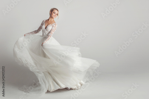 Beautiful attractive bride in wedding dress with long full skirt, white background, dance and smile