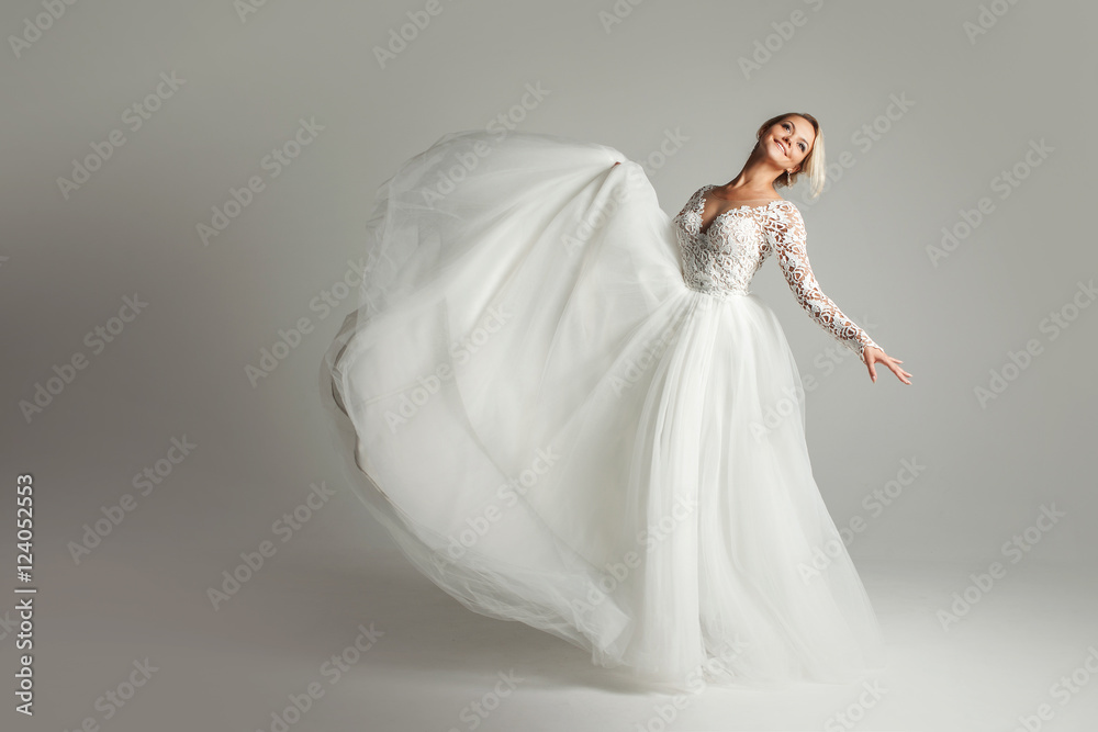 Beautiful attractive bride in wedding dress with long full skirt, white background, dance and smile Beautiful attractive bride in wedding dress with long full skirt, white background, dance and smile
