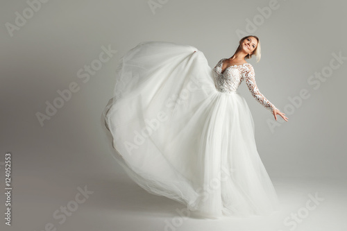 Beautiful attractive bride in wedding dress with long full skirt  white background  dance and smile