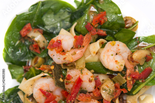 close up on fresh salad of prawns, pasta, baby spinach and chili, on white