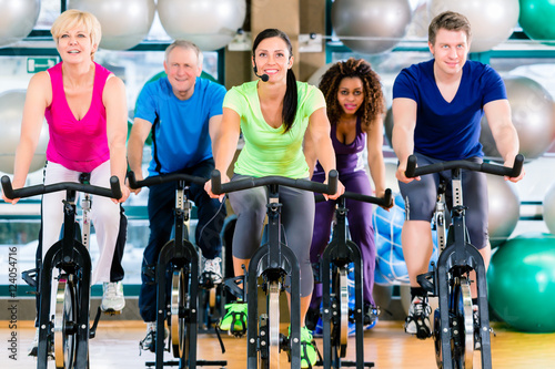 Fitness group of men and women spinning of bike in gym © Kzenon