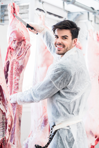 Butcher in butchery or slaughterhouse cutting meat