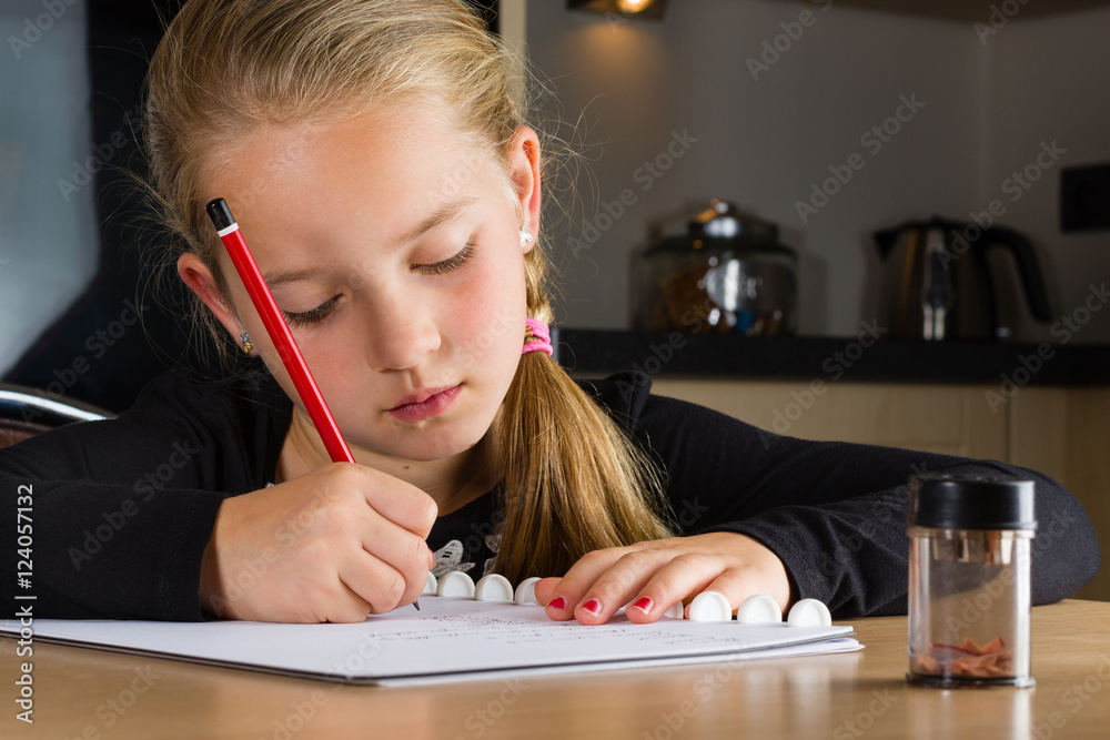 Young girl doing homework at home in the kitchen, writing a paper