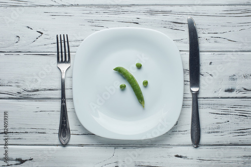 Pea pod and several peas on a white plate.
A little food on the plate. Fasting is a way to lose weight.
