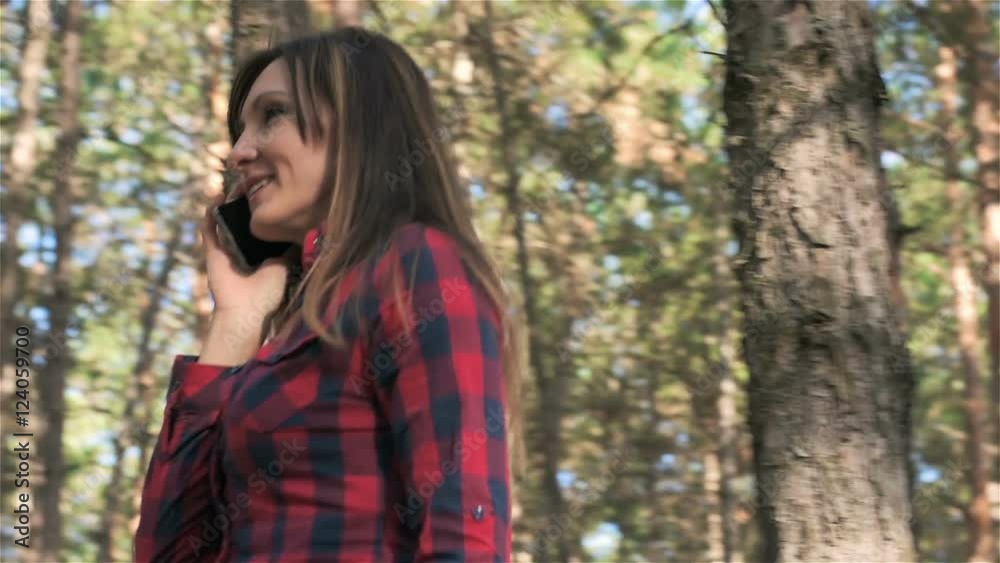 Happy woman talking on mobile phone and walking in circle. Young woman talking on mobile phone in pine forest Happy woman talking on mobile phone and walking in circle. Young woman talking on mobile phone in pine forest