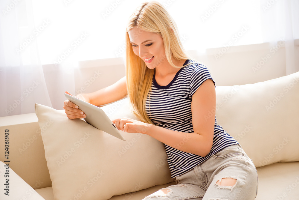 Young smiling woman having rest and sitting on sofa with tablet