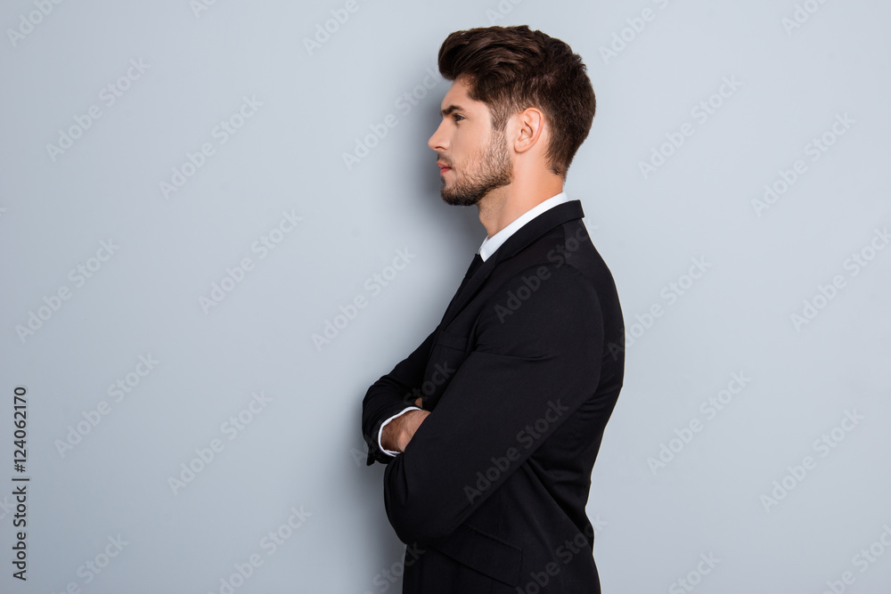 Side view of serious businessman with crossed hands on gray back Side view of serious businessman with crossed hands on gray back