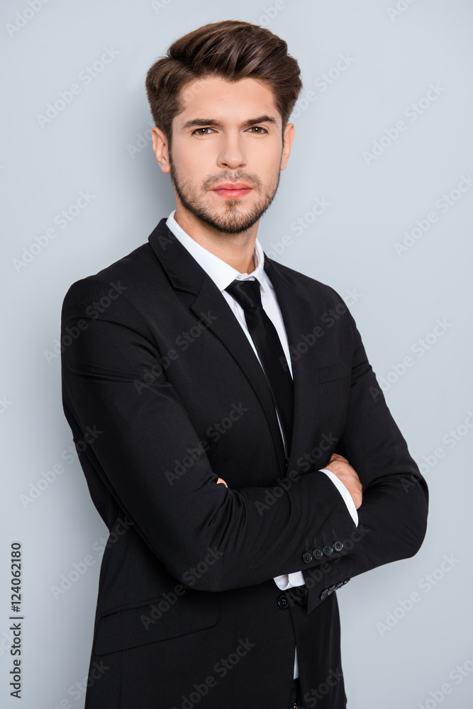 Portrait of serious young businessman in black suit with crosed