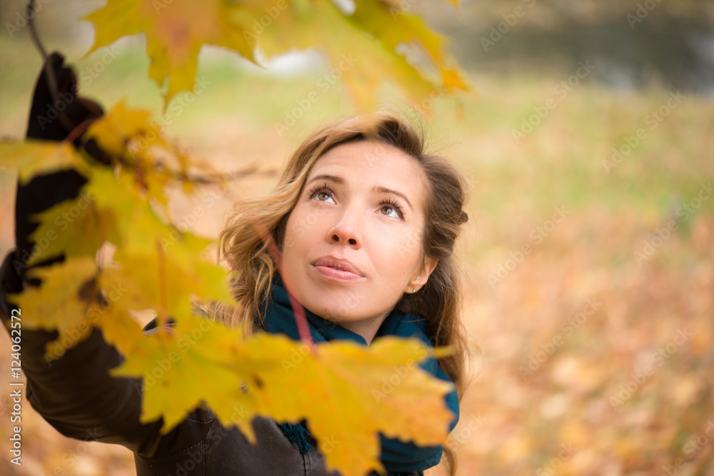 Beautiful girl blonde with wavy hair wearing a blue scarf standing at autumn tree with yellow leaves Beautiful girl blonde with wavy hair wearing a blue scarf standing at autumn tree with yellow leaves
