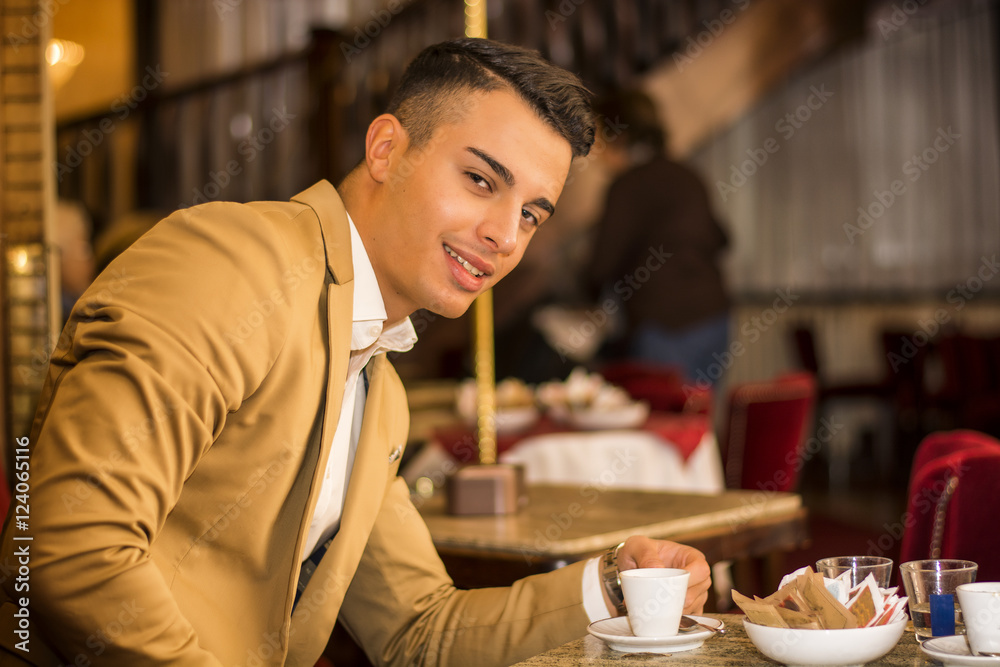 Portrait of smiling handsome man in jacket sitting at table with cup of drink looking at camera