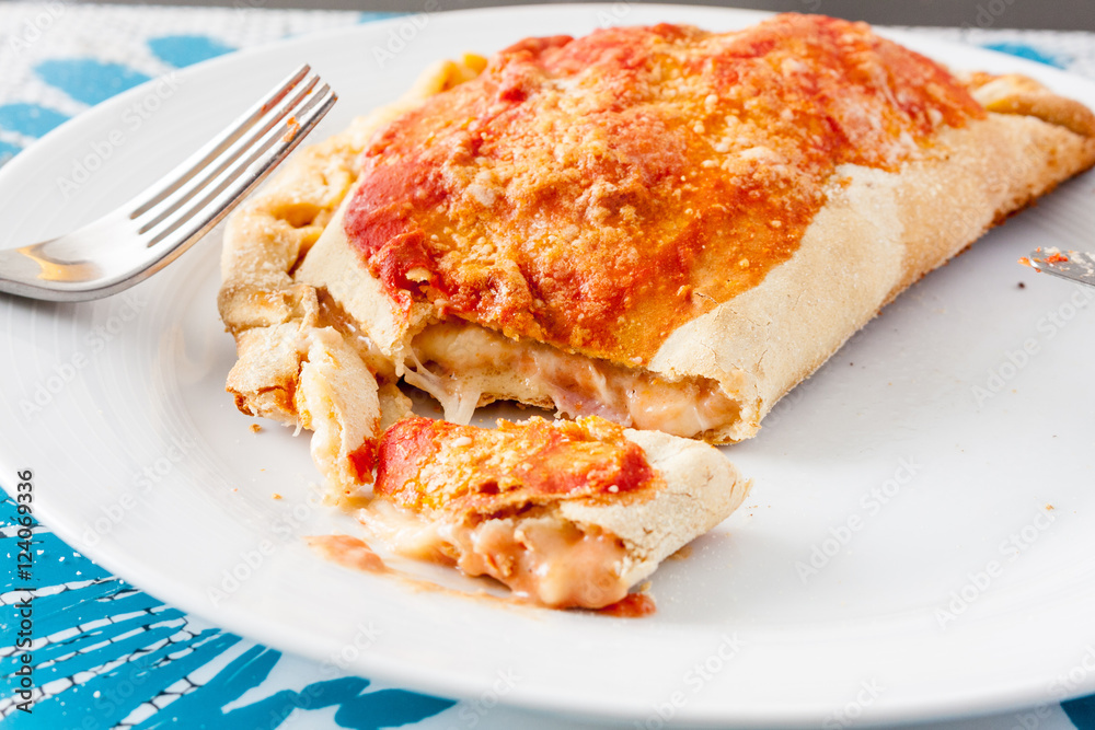 A cut open calzone, a type of folded pizza, showing the melted oozing cheese on a white plate