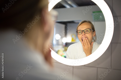 Groggy, young woman yawning in front of her bathroom mirror  photo