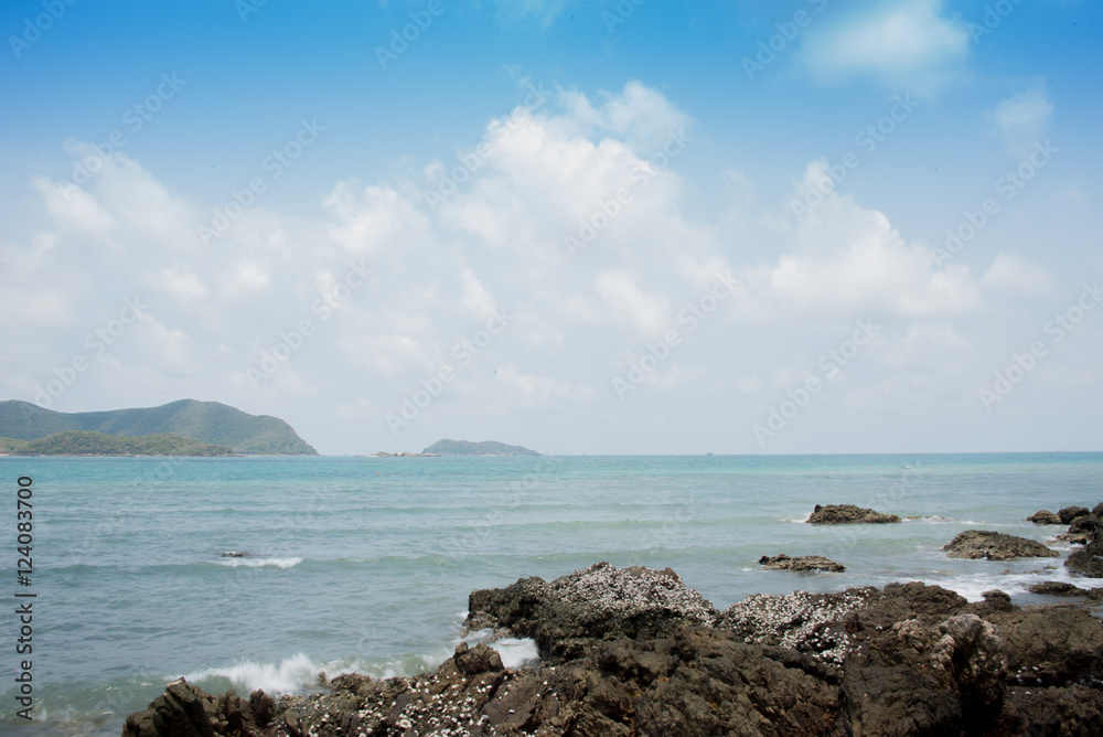 Sea waves crashing over rocks on wild stone beach , Thailand. Calm sea water,  Sattahip. White clouds on a blue sky over summer sea with sunlight reflection, Sattahip tropical sea relax