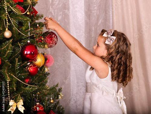 Child decorate on Christmas tree. Little girl getting dressed Christmas ball. photo