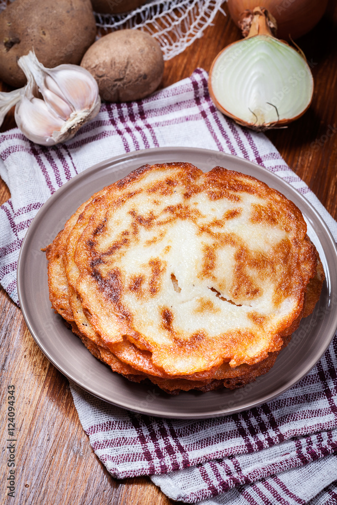 Stack of potato pancakes on a wooden table. In the background po Stack of potato pancakes on a wooden table. In the background po