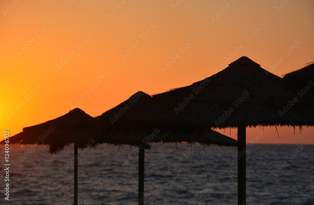 Tropical sunset with beach umbrellas and sea