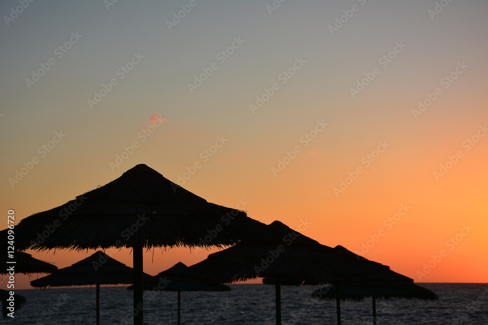 Tropical sunset with beach umbrellas and sea