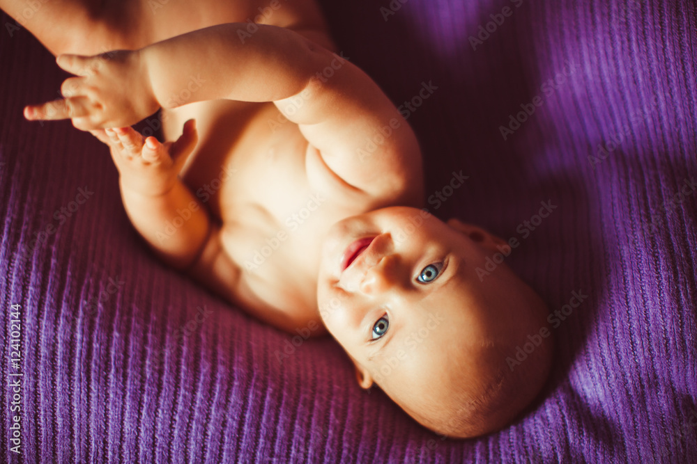 Happy naked blue-eyed kid lies on the violet blanket