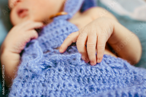 Little child sleeps under blue woolen blanket holding its hands