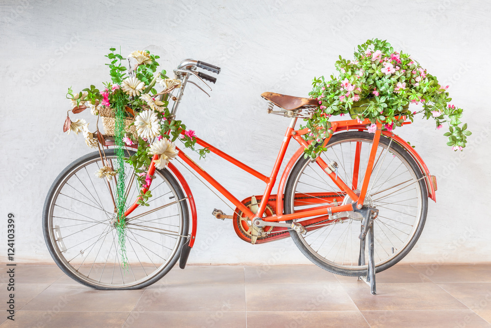 Vintage red bicycle with flower baskets parking against cement w