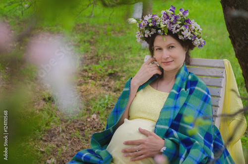 Pretty pregnant woman in a yellow dress and a wreath of flowers in spring blossoming apple orchard